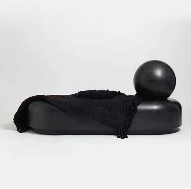 Black moulded daybed with a sphere at one end and a throw draped over it