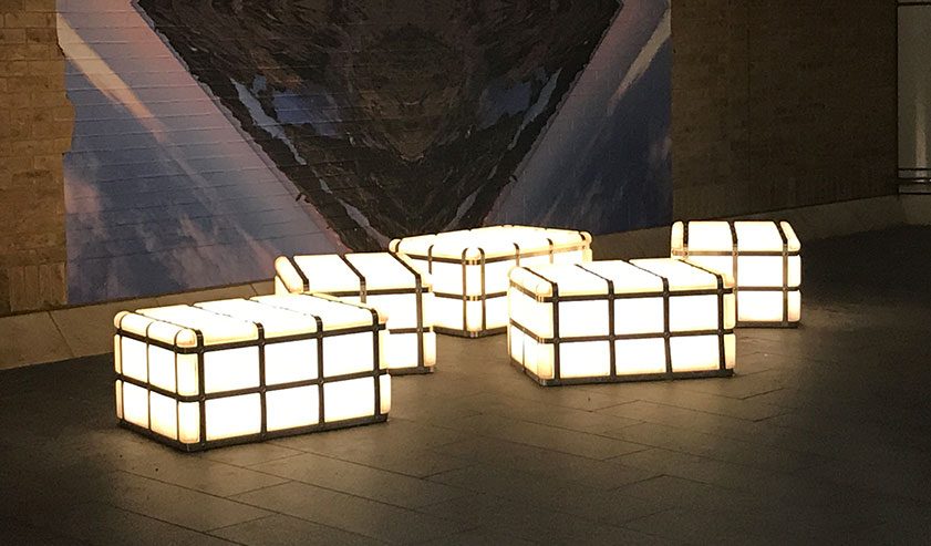 Five illuminated translucent blocks glowing on a paved floor
