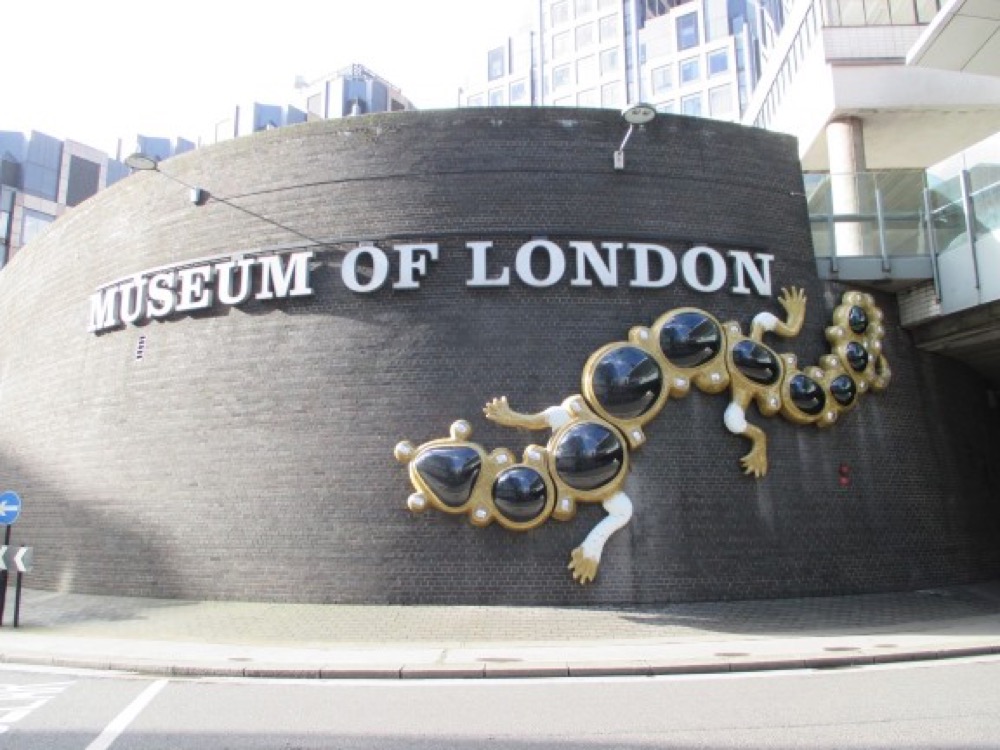 Gold sculpted frames with mirrored discs mounted on the curved outside wall of the Museum of London